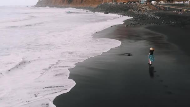 Tenerife'nin en iyi havadan görünümü. Şık giyimli kadın siyah kum üzerinde plaj boyunca koşmak, onun izleri arkasında. Kamera onu takip ediyor, Socorro plajının yukarıdan aşağıya bir görüntüsü. Kanarya Adaları, İspanya — Stok video