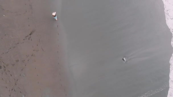 Vista de pájaro - una chica con sombrero corre a lo largo de la playa de arena negra. Tenerife, España — Vídeos de Stock