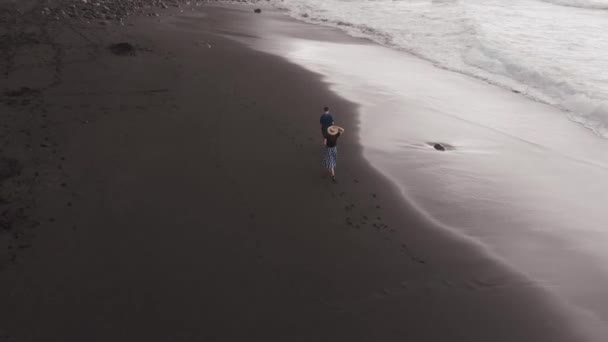 Widok z lotu ptaka na czarną plażę. Mężczyzna i kobieta szybko biegną na wulkanicznym piasku wzdłuż Oceanu Atlantyckiego na Teneryfie. Hiszpania — Wideo stockowe