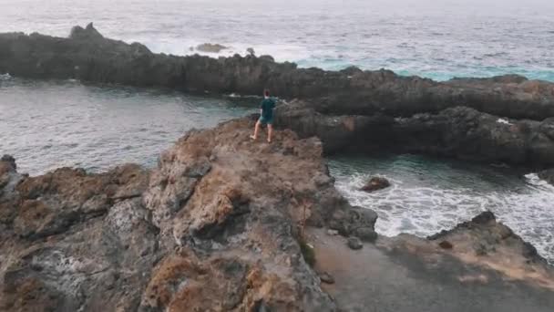 Dronen flyr over en mann som står på kanten av en vulkansk stein. Tenerife, Spania – stockvideo