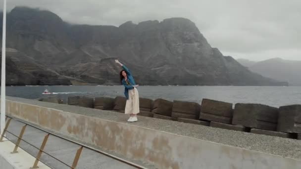 Vista aérea - una joven turista jugando contra el fondo del océano y las montañas brumosas. Agaete, Gran Canaria — Vídeos de Stock