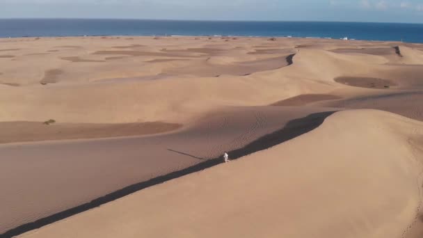 Une jeune fille caucasienne en vêtements d'été court le long du bord d'une dune dans le désert au coucher du soleil. Maspalomas, Grande Canarie 