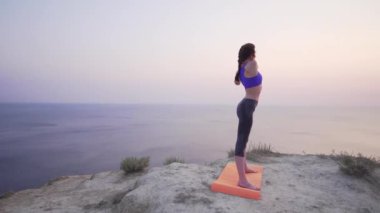 Gün batımında güzel ve ince bir kız spor yapıyor - açık hava eğitimi öncesi germe.