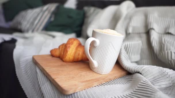 Καφές σε λευκό φλιτζάνι και φρέσκο κρουασάν σε έναν άνετο καναπέ. Πρωινό σε μια κρύα χειμωνιάτικη μέρα. Η έννοια της άνεσης, της ζεστασιάς και της φροντίδας — Αρχείο Βίντεο