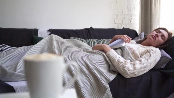 Menina branca bonita dormindo com um livro em suas mãos, escondendo-se em um cobertor. Relaxamento e lazer — Vídeo de Stock