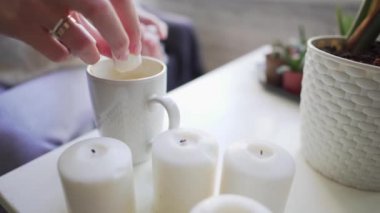 Hygge - mumlar ve kahve bardağı yakın çekim beyaz bir masada. Kız sıcak bir içecek için marshmallows ekler sıcak tutmak ve tadı zevk.