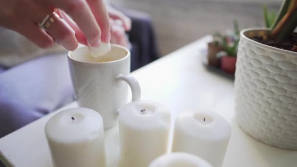 Hygge-svíčky a hrnek na kávu zblízka na bílém stole. Dívka přidává na horký nápoj Marshmallow, aby se udržel v teple a vychutnal si chutě. — Stock video