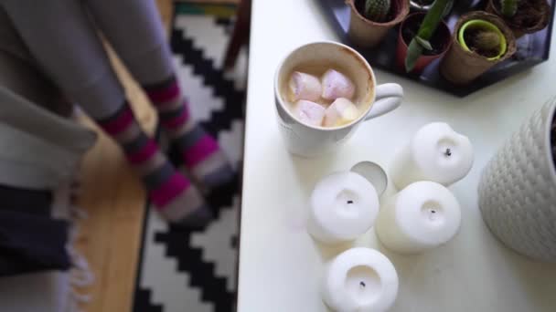 El concepto Hygge o Lagom - las velas, el café, los calcetines calientes sobre la alfombra hermosa sobre el suelo de madera. Mujer joven añade malvaviscos a café fresco — Vídeo de stock