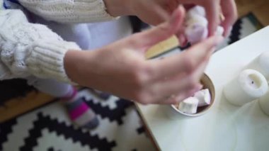 Close up - kadın mumlar yanında bir masaüzerinde duran beyaz bir kahve fincanı marshmallows koyar
