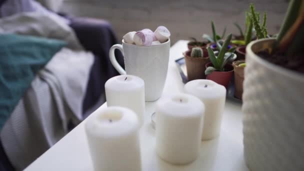 Odpočiňte si na zimních prázdninách-šálek horké čokolády s Marshmallow na bílém stole, svíčky na domácích rostlinách za studeného zimního dne — Stock video