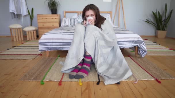 Hygge concept - beautiful attractive girl sitting, wrapped in a cozy blanket on the floor in her bedroom and resting — Stock Video