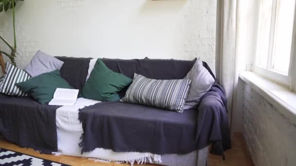 Sofá acogedor suave y hermoso con un libro, almohadas, cuadros y manta. Concepto Lagom — Vídeo de stock
