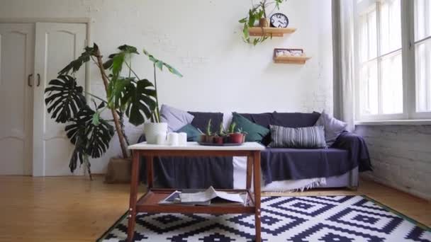 Um belo tapete, uma pequena mesa com revistas, um sofá aconchegante contra a parede branca. Apartamentos Loft — Vídeo de Stock