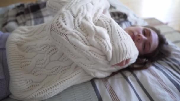 Happy Caucasian young woman basking at home on a cold autumn evening, smiling and looking at the camera. White woolen knitted sweater closeup, hugge concept — Stock Video