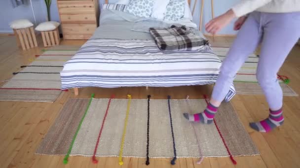 Een vrouw in huis kleren loopt op een gebreide bed deken en corrigeer haar bruin-roze Sok. — Stockvideo
