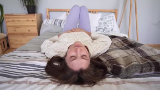 Jeune femme heureuse aime se détendre pendant les vacances d'hiver, vêtements chauds confortables, lit avec couvertures, un plaid et des oreillers — Video