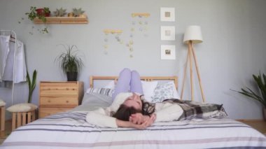 Statik çekim - beyaz örme kazak güzel bir çekici kadın baş aşağı rahat bir yatakta yatıyor ve saçlarını düzleştirer. Lagom veya Hygge kavramı