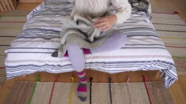 Lagom konsepti. Pijama ve çok renkli örme çorap bir kız yatakta oturur ve rahat bir ekose kendini sarar.