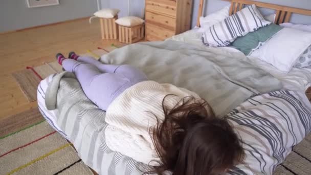 Een vrouw valt op een gezellig bed na een harde dag en wikkelt zich in een deken. — Stockvideo