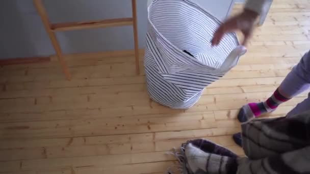 Uma mulher coloca um cobertor de lã em uma cesta de lavanderia, em um fundo de um chão de madeira. Trabalhos domésticos — Vídeo de Stock