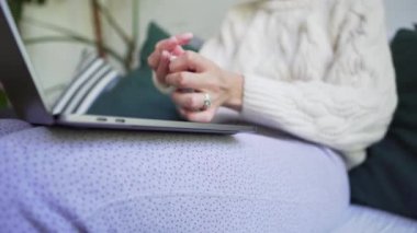 Bir kadın evde donuyor, kendini beyaz örme bir kazakla sarıyor ve dizüstü bilgisayarda çalışıyor. Hygge kavramı. Close