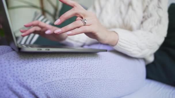 El primer plano - la muchacha en el pijama y el jersey blanco que escribe en el portátil. Trabajar en casa, con comodidad y calidez — Vídeos de Stock