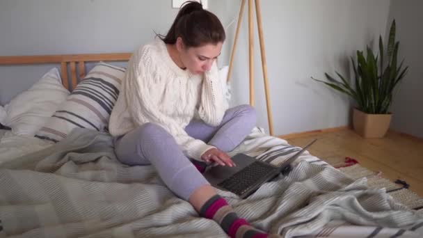 Μια νεαρή επιχείρηση που δουλεύει στο κρεβάτι και κάθεται με ένα λάπτοπ. Ηλεκτρονικό εμπόριο από οπουδήποτε — Αρχείο Βίντεο