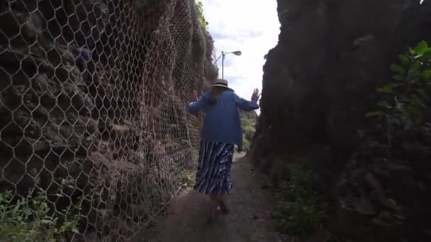 Mladá žena se bojí klaustrofobie a běží v uličce mezi horami. Mřížka pro ochranu proti kolapsu, hory na pobřeží španělského ostrova v Atlantickém oceánu — Stock video