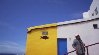 El Pris, Tenerife, İspanya - 16 Nisan 2019: Okyanus kıyısındaki eski bir balıkçı İspanyol kasabasında parlak renkli bir evin arka planında iki adam.