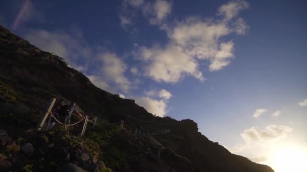 Chica con estilo va por el acantilado al atardecer. Escaleras empinadas frente a la costa del Océano Atlántico, descenso a la playa salvaje de Benijo. Accesibilidad y comodidades para los turistas — Vídeos de Stock