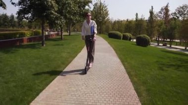 Çekici genç beyaz beyaz kadın hareket halinde çekilmiş bir scooter'ı kontrol ediyor. Doğada ve yeşillikte ekolojik elektrik tipi ulaşım