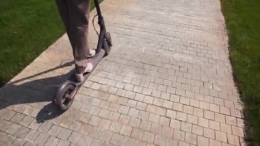 Hipster yöneticisi kız bir elektrikli scooter üzerinde çalışmak için sürmek, bacaklar closeup. Modern bir şehirde yoğun saat ve trafik sıkışıklığı sırasında sürüş için çevre dostu gadget.