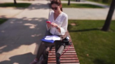 Elinde bir akıllı telefon ile Kadın hipster bir elektrikli bisiklet direksiyon arka plan karşı, Internet üzerinden bir satış yapar.