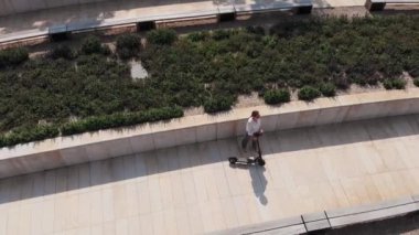 Gözlük ve iş kıyafetleri genç bir iş kadını bir öğle yemeği molası için bir elektrikli scooter yanında duruyor. Bir insansız hava aracından sokak atışı