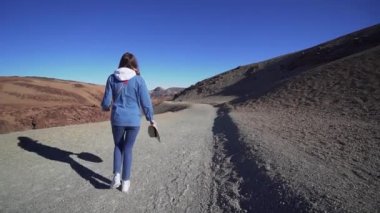Kot ve elinde bir şapka bir kız volkanik ve ıssız arazi dağlarda yüksek boyunca yürüyor. Geniş açı, sloumo.