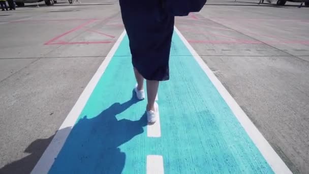 The girl is landing on an airplane on a strip at the airport, legs in a dress and a backpack close-up — Stock Video