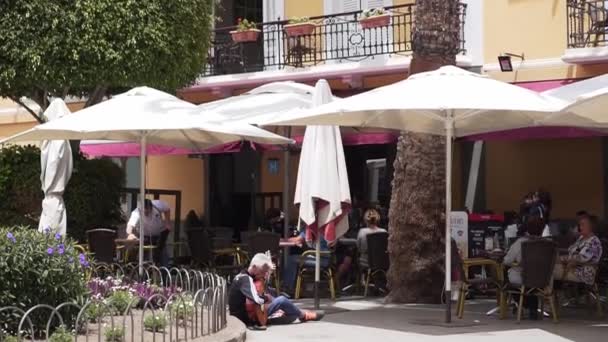 Las Palmas de Gran Canaria, ESPANHA - 23 de abril de 2019 - Um músico de rua se senta no chão e toca guitarra em um restaurante ao ar livre. Artista num café de rua na Europa, pobreza e mendicidade — Vídeo de Stock