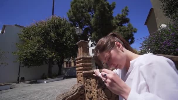 Atractiva mujer joven caucásica despega y se pone gafas elegantes mientras está sentado en un banco tallado hecho de patrones. Descanso durante el turismo, vacaciones de verano — Vídeos de Stock