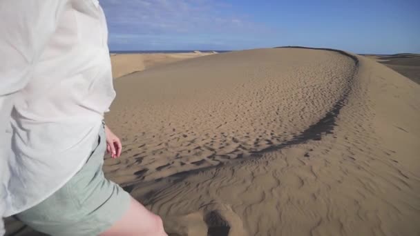 Een gelukkige vrouw in casual kleding loopt langs een hoge duin in de woestijn aan de kust van de Atlantische Oceaan. Lifestyle concept. Alleen meisje in de woestijn — Stockvideo