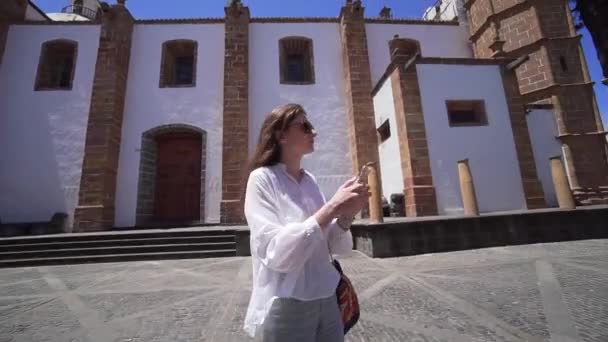 彼女の手に携帯電話を持つ観光客は、スペインの街の通りに観光スポットや古代の建築物を撮影します。休暇中のストリートツアー — ストック動画
