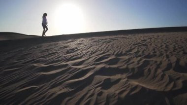 Gün batımında çölde kumul boyunca yürüyen güzel bir kızın silueti. Maspalomas Çölü, Gran Kanaryası, İspanya