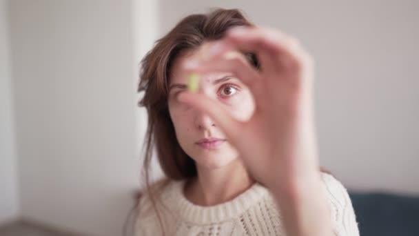 Une belle femme caucasienne prend une pilule vitaminée et la regarde, la tenant devant ses yeux. Santé et traitement médical, santé et médecine concept — Video