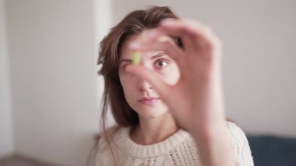 Una hermosa mujer caucásica toma una píldora vitamínica y la mira, sosteniéndola frente a sus ojos. Salud y tratamiento médico, concepto de salud y medicina — Vídeos de Stock