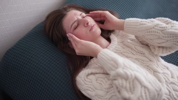 The woman experiences a headache, rubs her temples and frowns in pain. Seasonal disease, Caucasian girl in the bedroom on sick leave — Stock Video