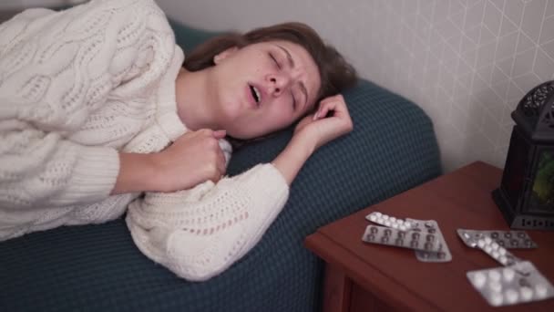 A woman coughs and clings to her neck. The girl has a sore throat and frowns. Medications and pills lie on a side table — Stock Video