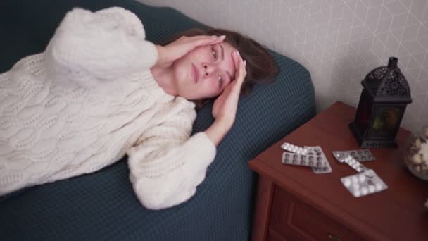 An ill woman looks at the camera and clings to her head, experiencing a headache. Flu disease. Infection and temperature — Stock Video