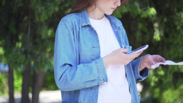 Escaneo QR. La chica escanea el código en un cheque de la tienda, afuera — Vídeos de Stock