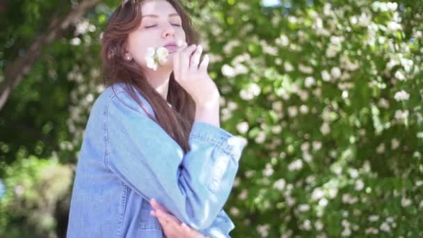 Χιλιετηρίδα κορίτσι με λουλούδι. Γυναίκα σε ένα τζιν σακάκι απολαμβάνει τη ζωή και κρατά στο χέρι της ένα όμορφο λευκό λουλούδι γιασεμί, copyspace — Αρχείο Βίντεο