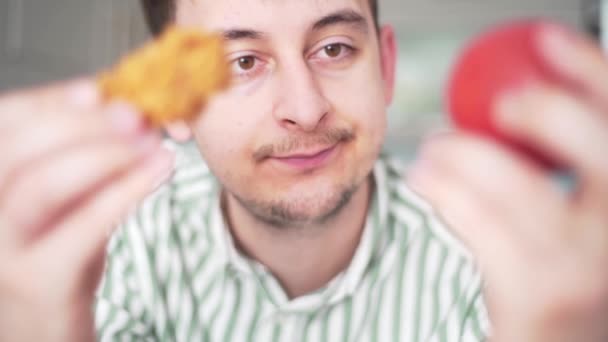 L'homme choisit entre des aliments malsains et sains. Le gars tient la tomate et le poulet croustillant et choisit entre eux. Régime alimentaire ou obésité, mode de vie malsain — Video