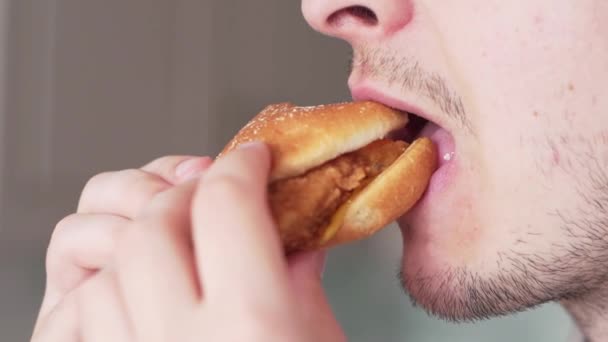 Człowiek je śmieciowe żarcie, zbliżenie. Gość powoli gryzie hamburgera. — Wideo stockowe